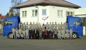 25 Jahre Partner der MAN. Team des Autohauses mit Geschäftsführung posiert vor dem Firmengebäude mit zwei moderne LKWs