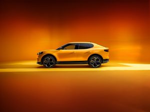 Gelber Ford Capri im Profil vor orangefarbenem Hintergrund – ikonisches Coupé mit sportlicher Silhouette, charakteristischen Doppelscheinwerfern und markanter Seitenlinie.